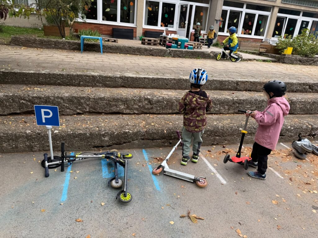 Dvě děti parkují koloběžky na nakresleném parkovišti u dopravní značky P.