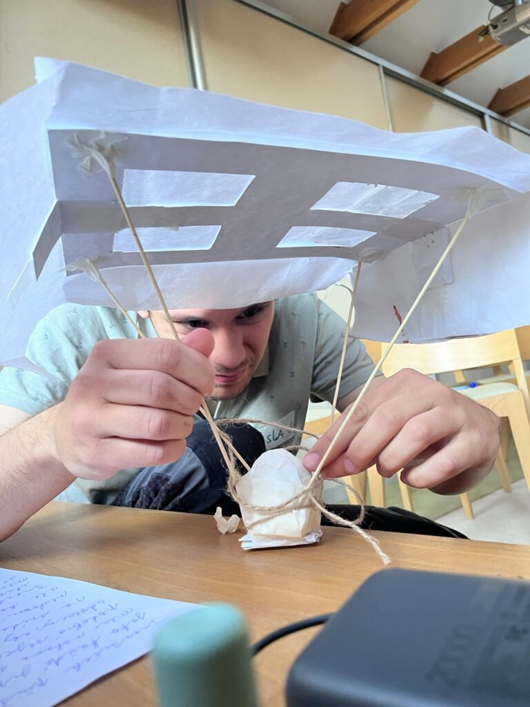 Žák napjatě skládá z papíru, špejlí a provázku padák pro vajíčko při týmové výzvě.