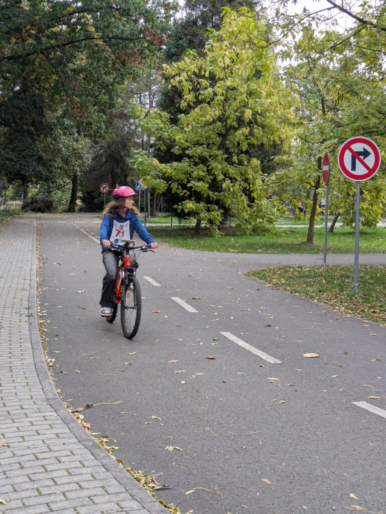 Soutěžící v růžové přilbě jede na kole po dopravním hřišti.
